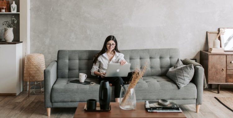 Girl works on her laptop while she is sitting on a couch.